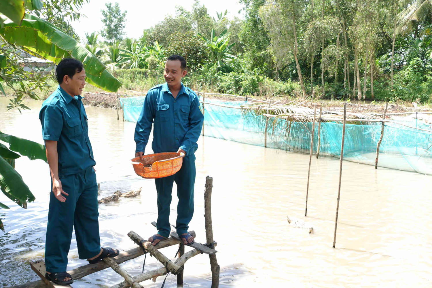 Cán bộ Ban Chỉ huy Quân sự xã Vĩnh Hòa Hưng Bắc thăm mô hình nuôi cá của anh Phan Ngọc Quý (bên phải).